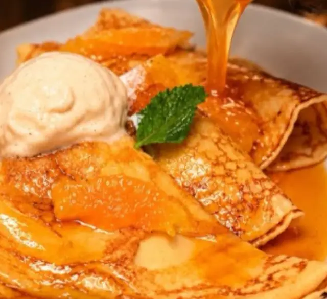 Crepes Suzette with orange syrup poured over and a scoop of ice cream